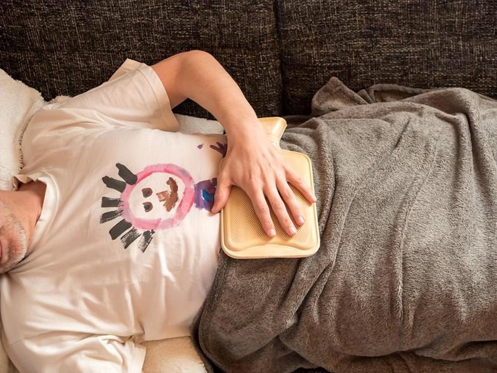 A person resting under a blanket with a warm pad on the belly